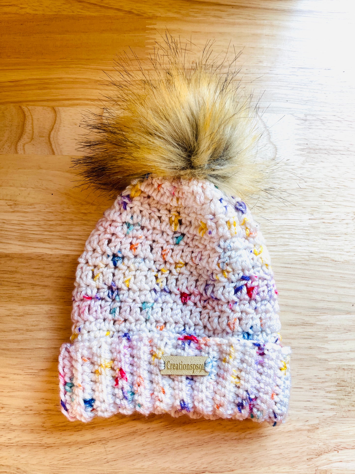 Pink crocheted beanie and yarn on a wooden surface, made with 100% premium acrylic yarn, circumference 14" with stretch 16" washable and tumble dry 