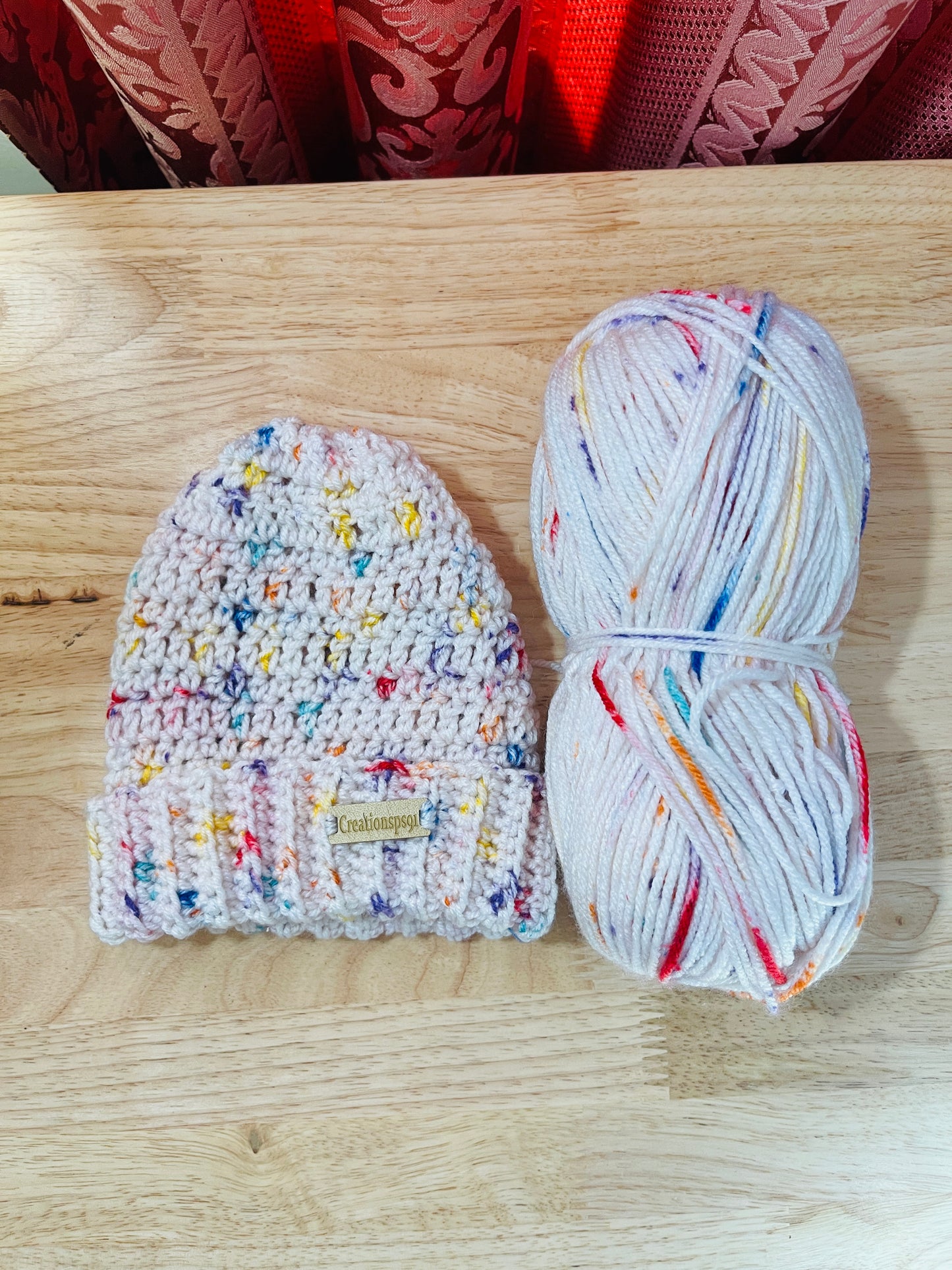 Pink crocheted beanie and yarn on a wooden surface, made with 100% premium acrylic yarn, circumference 14" with stretch 16" washable and tumble dry 