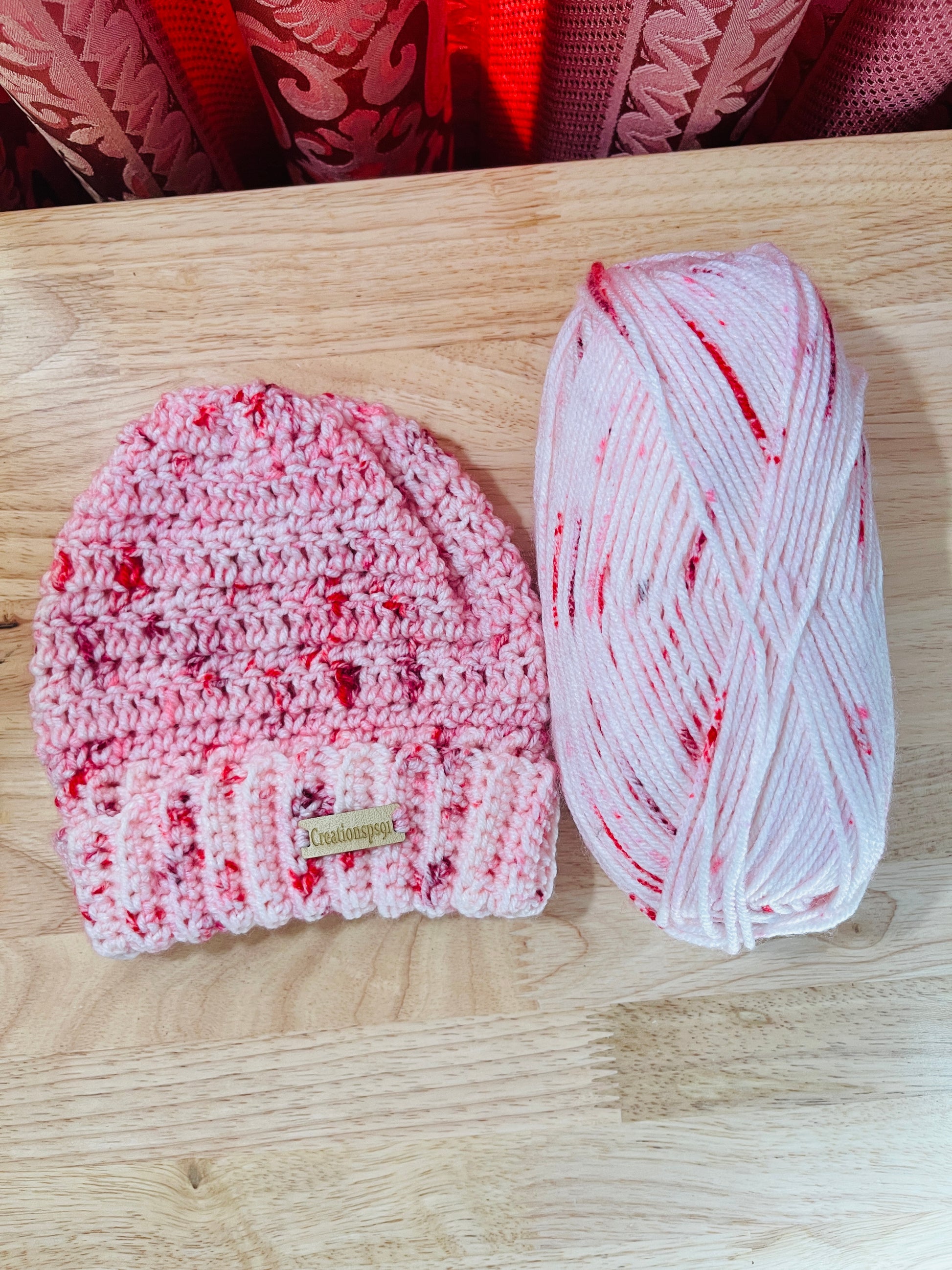 Pink crocheted beanie and yarn on a wooden surface, made with 100% premium acrylic yarn, circumference 14" with stretch 16" washable and tumble dry 