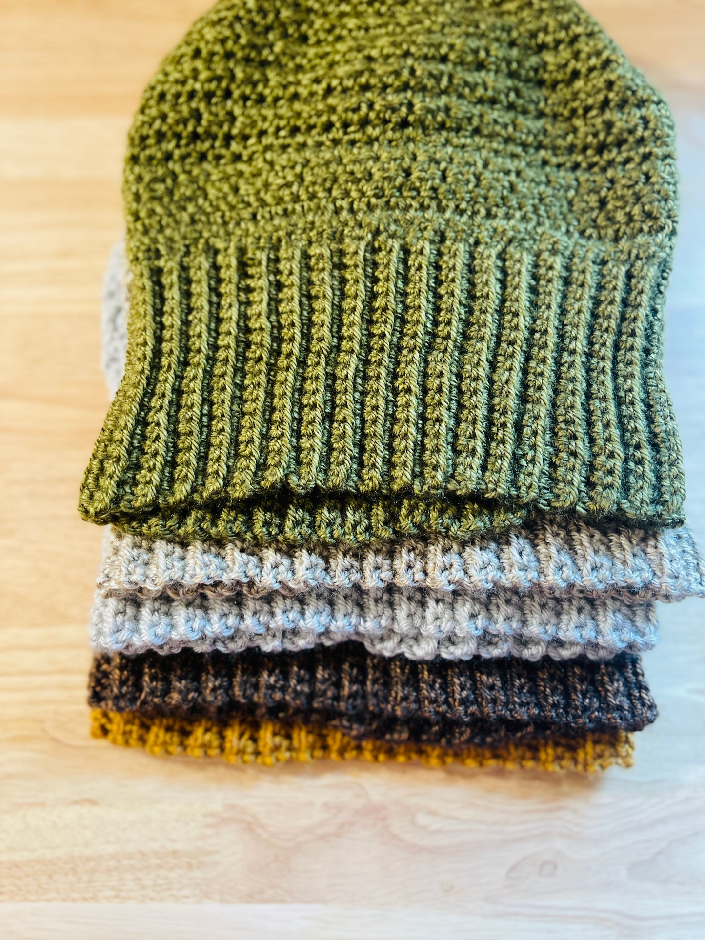 Beanies Stack on a wooden surface top of each other the colors are green, gray, brown, beige, sliver, and gold
